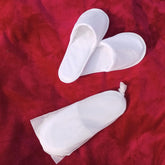 A pair of white carpet slippers for men and women displayed on a red surface.